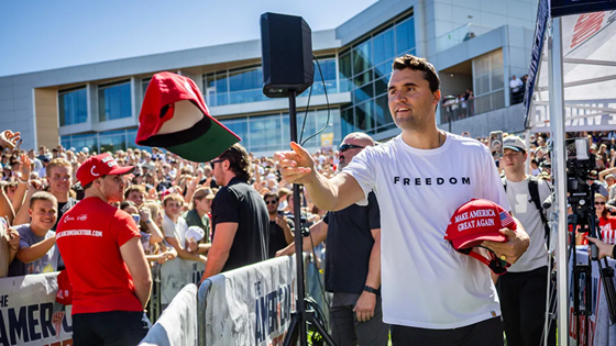 Charlie Kirk tossing a red "Make America Great Again" hat to a crowd at a rally